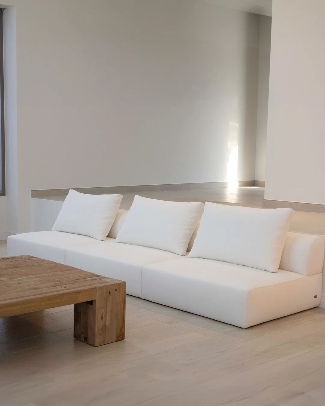 Modern white sofa with wooden coffee table in a minimalistic room.