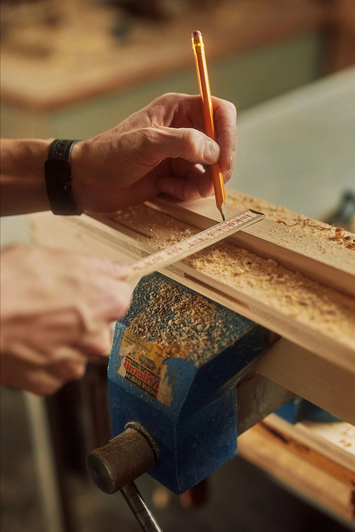 Person measuring a piece of wood with a pencil and ruler in a workshop.